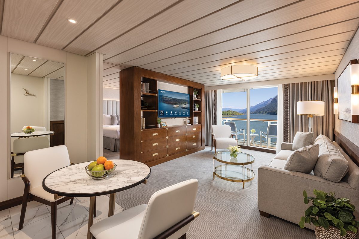 A Grand Suite aboard American Encore with a sitting area, dining table, bedroom beyond and floor-to-ceiling windows onto the river