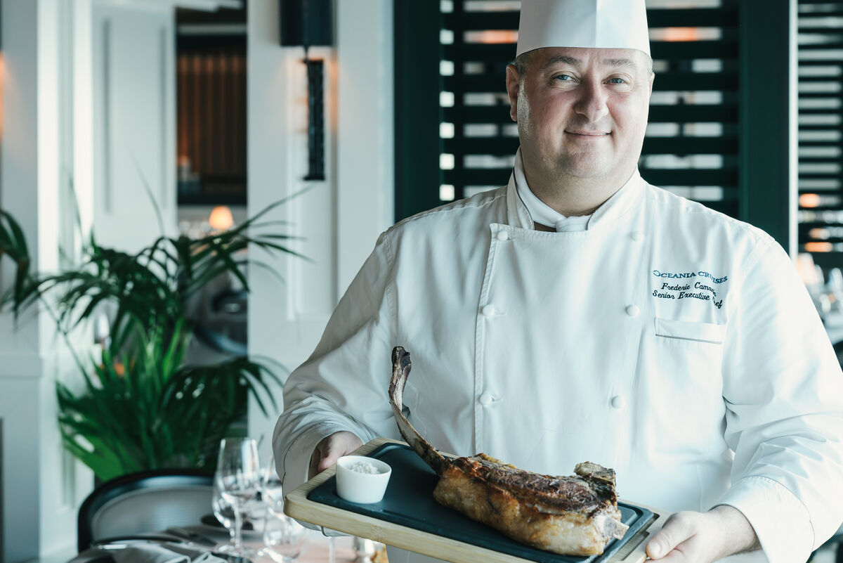 A chef in whites presents a carved tomahawk steak at Polo Grill aboard Oceania Vista